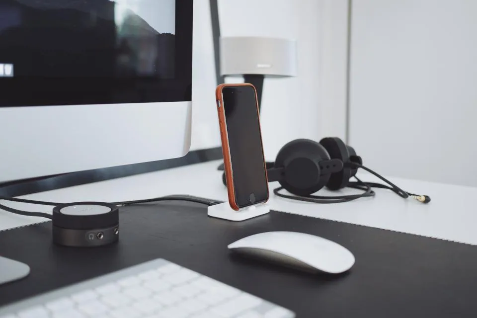 A tidy desk with a keyboard, a phone on a stand and a headset beside a monitor