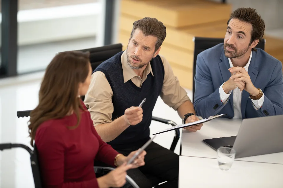 Three colleagues working through a plan at an office table, one holding a clipboard